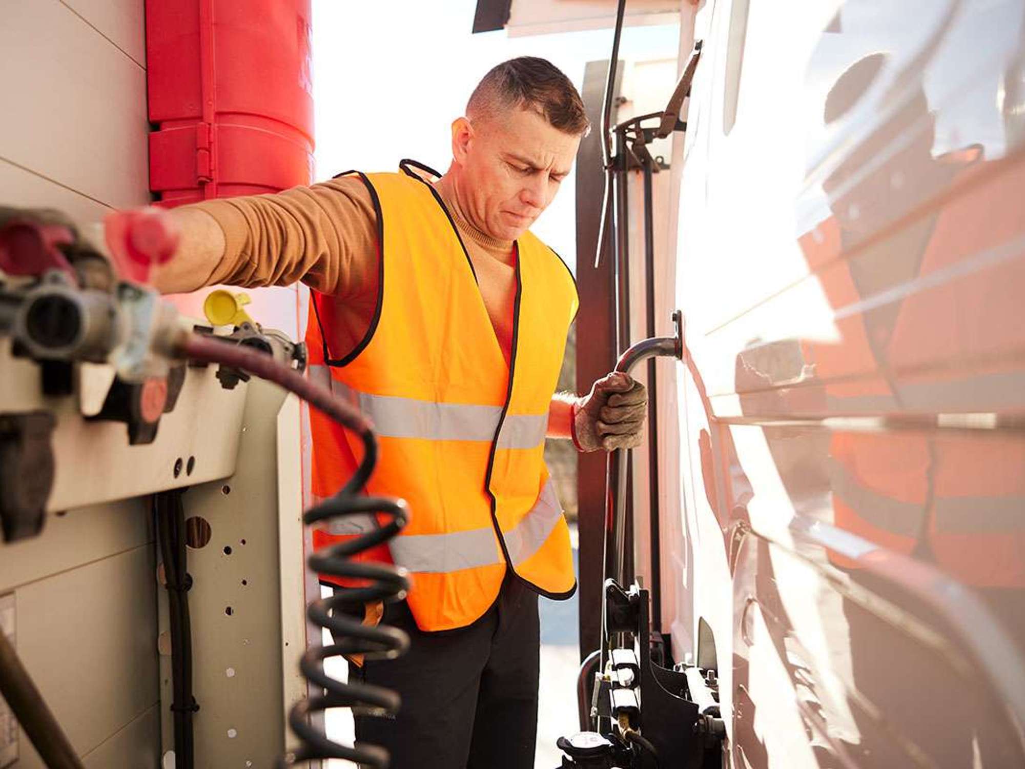 Truck driver in an orange vest and gloves examining semi-truck trailer brake coil for safety