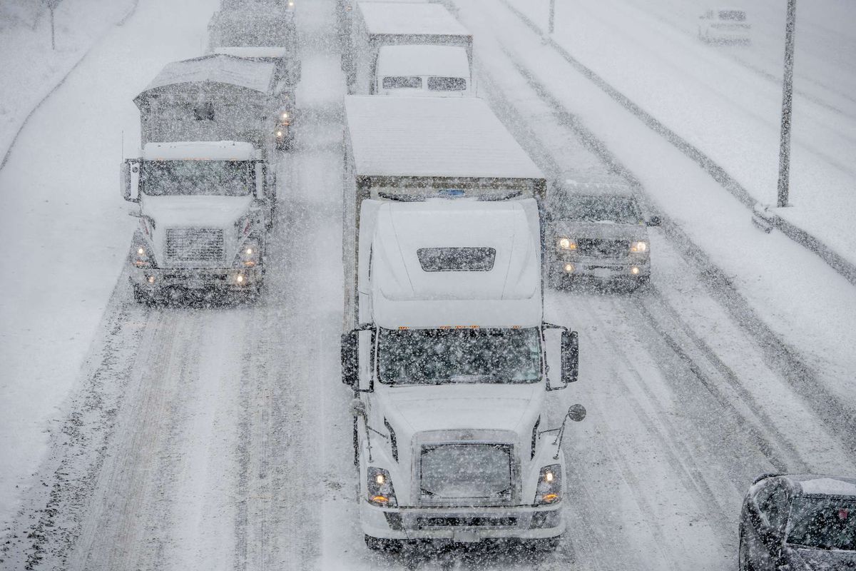 Trucks and cars drive on very snowy roads while it snows.
