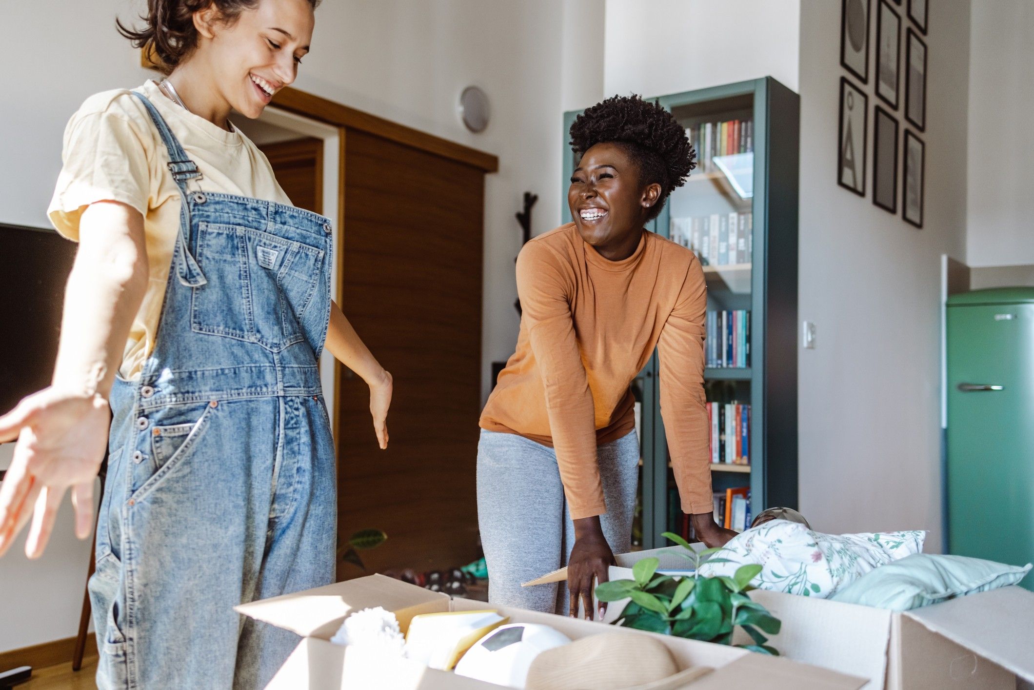 Two female college students pack belongings into boxes in their apartment.