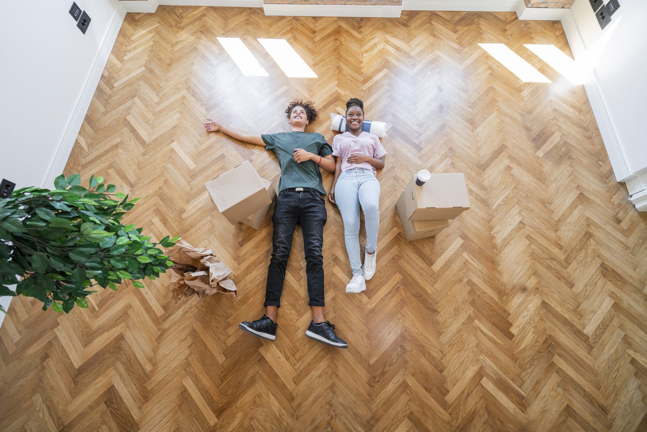 Two people lay in the middle of an empty room surrounded by a few moving boxes.