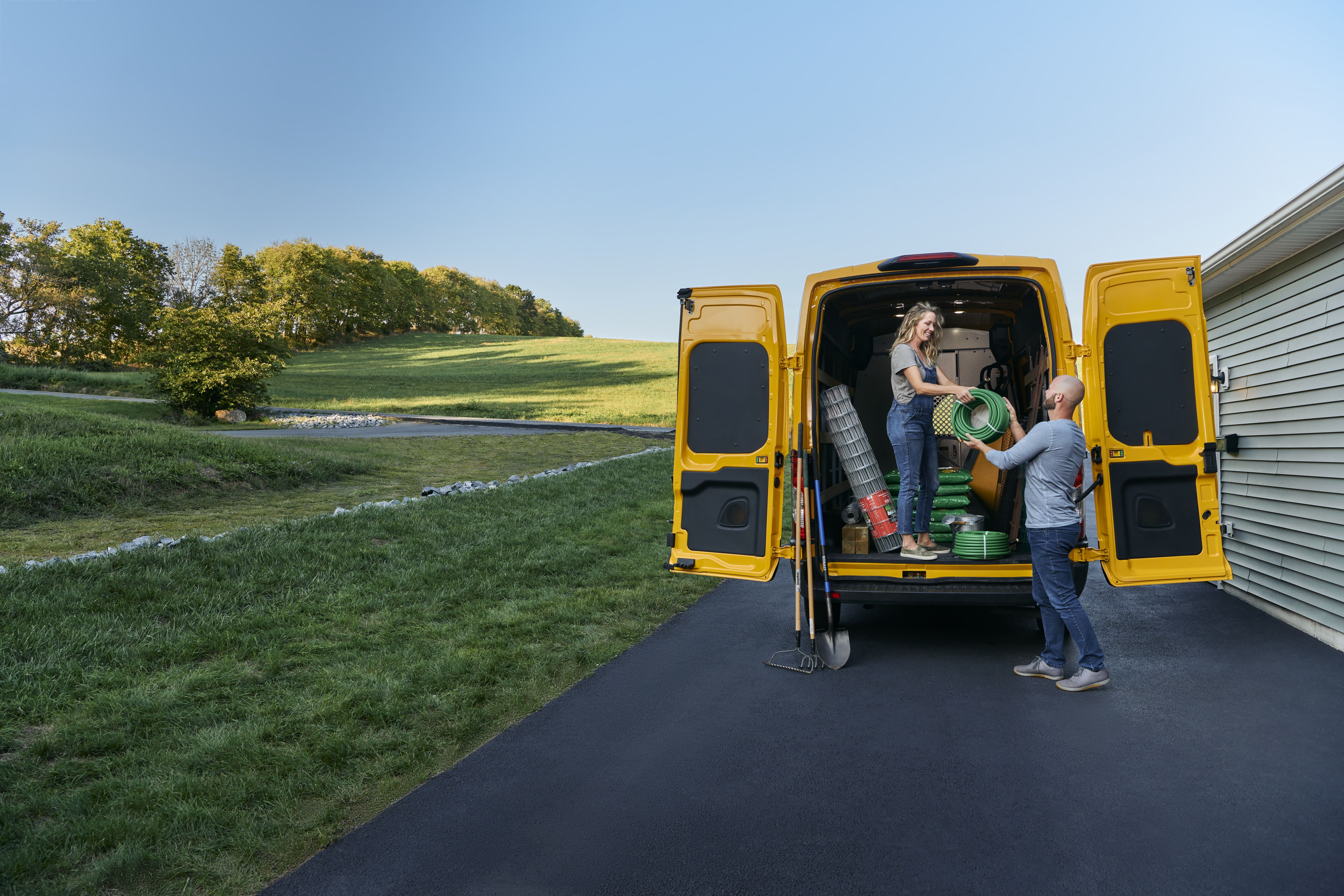 Two people unload gardening supplies from the back of a yellow Penske van.
