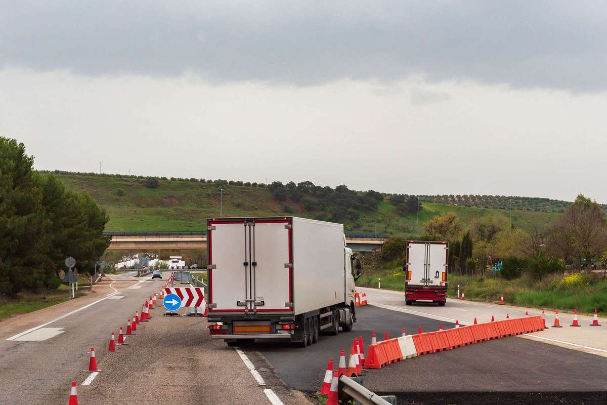 Two semi-trucks drive through a construction zone on a freeway.