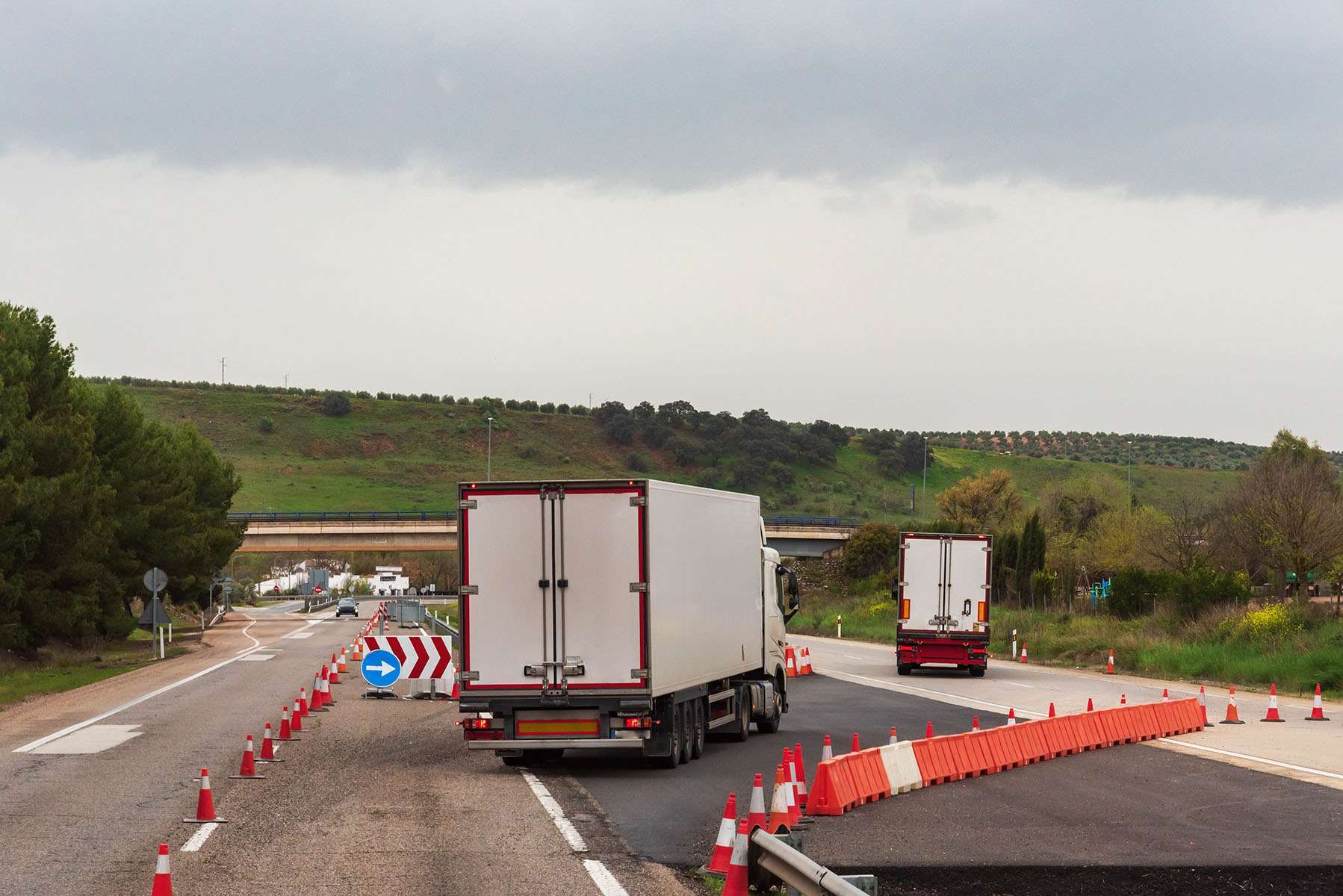 Two semi-trucks drive through a construction zone on a freeway.