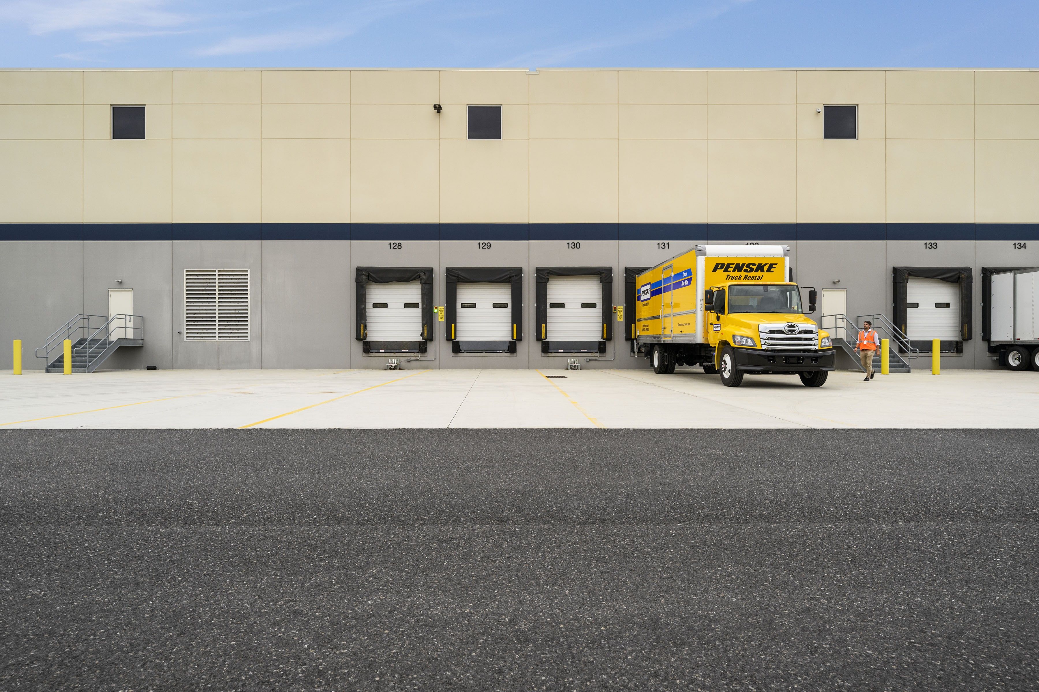 Two yellow Penske box trucks parked in a loading/unloading dock.