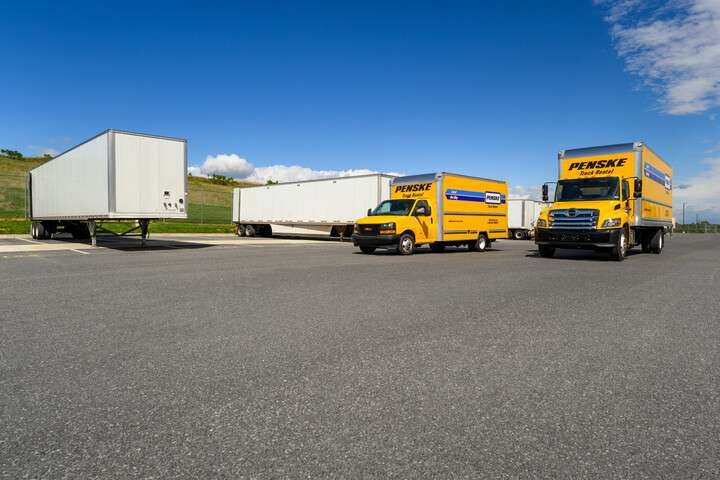 Two yellow Penske trucks parked in front of multiple white semi-trailers.