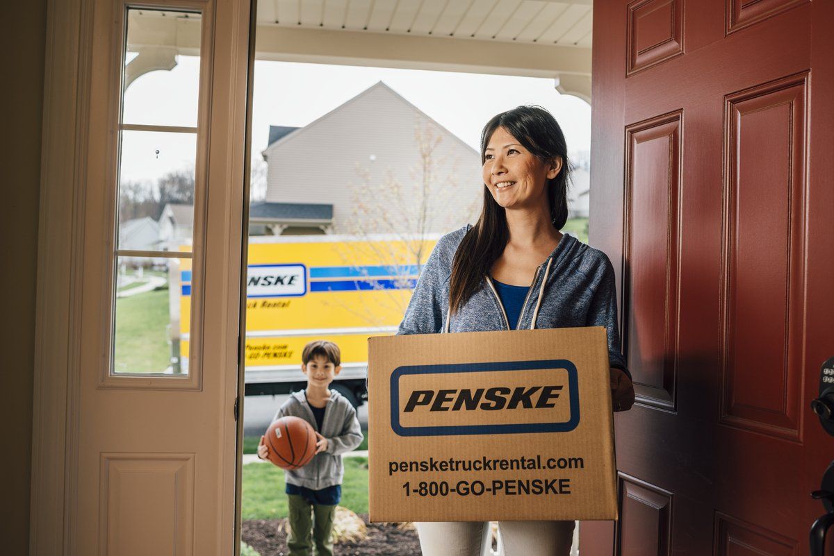 Woman walking through front door carrying a moving box.