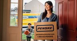 Woman walking through the front door carrying a Penske box