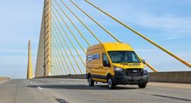 Yellow Penske van driving over bridge.